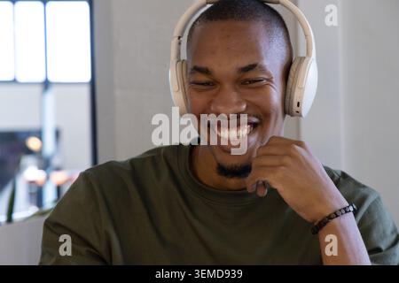 African American adult man smiling at desk in office with white headphones and bracelet by chin Stock Photo