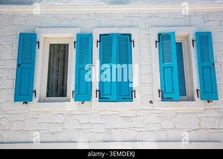 White painted stone facade with bright turquoise shutters framing two windows, Mediterranean architecture background with clean lines, symmetry, and s Stock Photo