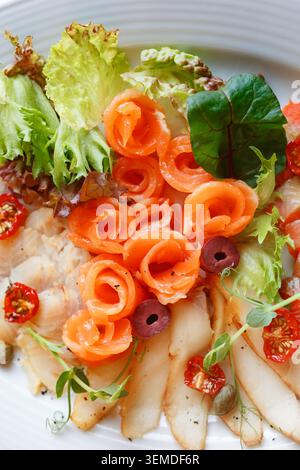 Close-up of a fresh salad plate with smoked salmon rosettes, sliced chicken, mixed lettuce, cherry tomato, olives, and herbs, served as a healthy lunc Stock Photo
