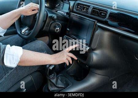 Close-up of a driver pressing the hazard warning button on a modern car dashboard, showing steering wheel and touchscreen console, highlighting safety Stock Photo