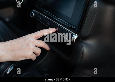 Close-up of a driver’s hand pressing the hazard warning button on a modern car dashboard, highlighting vehicle safety, emergency signal activation, an Stock Photo