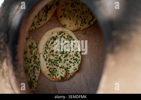 Close-up view inside a clay tandoor oven with traditional Uzbek bread rounds topped with herbs, freshly baked in Uzbekistan, showcasing Central Asian Stock Photo