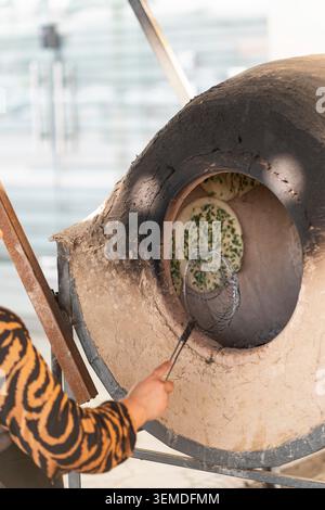 Close up of traditional Uzbek naan bread baking inside a clay tandoor oven, with a cook using a metal hook. Authentic Central Asian street food prepar Stock Photo