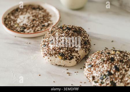 A close-up of freshly made sourdough bread loaves covered in a variety of seeds, placed on a lightly floured surface. Perfect for homemade and artisan Stock Photo