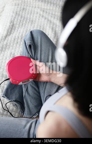 Overhead view of a person holding a portable CD player while wearing headphones, capturing Y2K aesthetic and retro audio gear for analog media revival Stock Photo