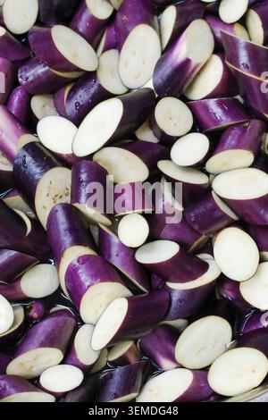 Close-up of fresh sliced eggplant pieces with purple skin, ready for restaurant meal prep, cooking, and menu service; clean raw vegetable background. Stock Photo