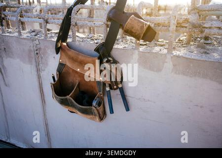 Close-up of a construction worker tool belt with hammer and hand tools resting on a concrete wall at a building site, highlighting craftsmanship, safe Stock Photo