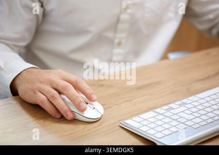A professional in a white shirt uses a wireless mouse, working efficiently at a modern wooden desk with a matching keyboard, symbolizing business and Stock Photo