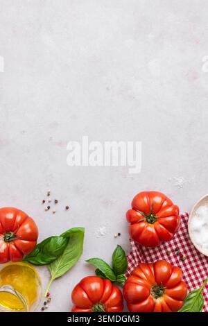 Juicy, ripe tomatoes paired with fresh basil leaves sit on a red and white checkered cloth. The scene is set with scattered peppercorns, salt, and a j Stock Photo