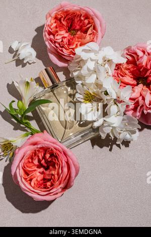 Flat lay of an elegant perfume bottle surrounded by pink roses and white flowers on a soft background, capturing fragrance, aroma and fresh smell in a Stock Photo
