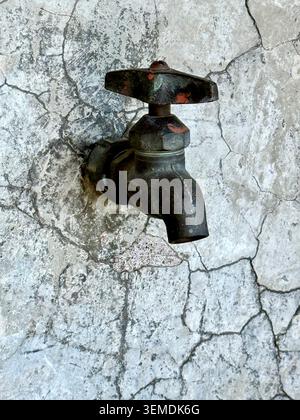 Dry old water tap on a cracked wall, a conceptual image illustrating water scarcity, drought and the global water crisis Stock Photo