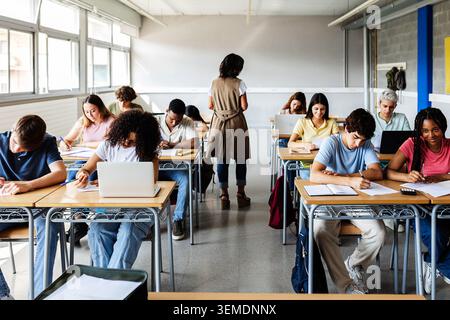 Diverse students learning in secondary school classroom with teacher Stock Photo