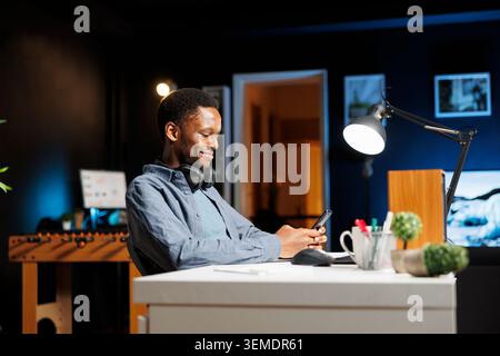 African american man texting on mobile device while he listens to trainer on online e learning course, navigating social media apps and attending internet training program. Student works from home. Stock Photo