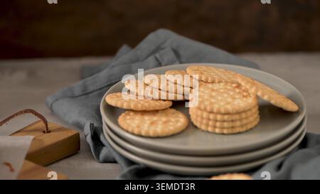 Crisp and golden round savory crackers arranged on a stack of grey plates with a blue fabric napkin. The rustic kitchen scene features warm lighting a Stock Photo