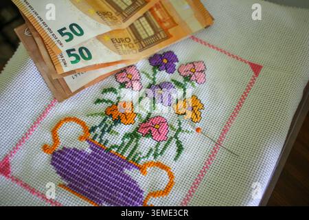 A high angle, close up shot depicting the cost of leisure activities, featuring a stack of fifty euro cash bills resting on a handmade canvas with col Stock Photo