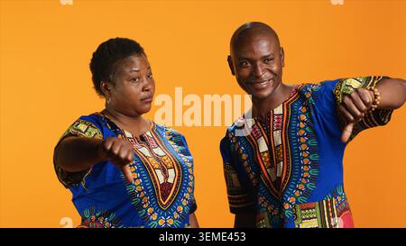 African american couple showing thumbs down sign, giving dislike symbol in front of camera and expressing disagreement. Negative man and woman presenting disapproval and bad review. Stock Photo