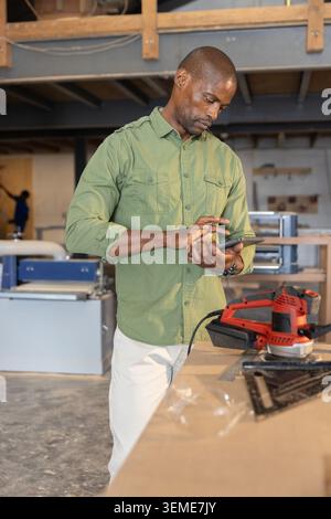 Mature African American man using digital tablet at workbench with red power sander in workshop Stock Photo