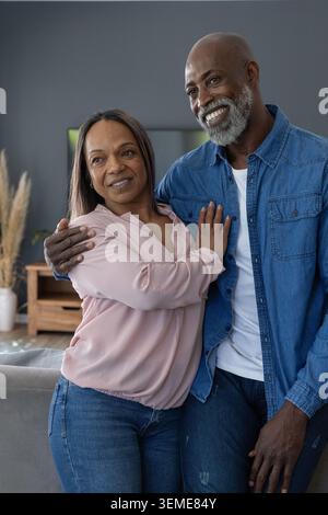 Diverse couple standing close in living room near wooden console and TV, man wearing denim Stock Photo