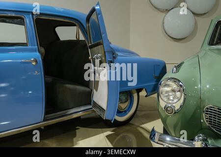 Close-up view of vintage blue sedan with open driver's side door, showcasing dark patterned seat. Adjacent, a lighter green vintage car's front fender Stock Photo