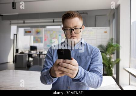 Young man with Down syndrome using mobile phone in office Stock Photo