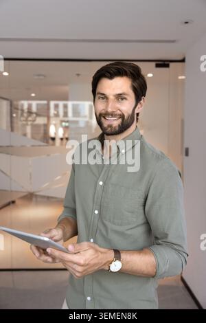 Businessman standing alone in modern workspace with digital tablet Stock Photo