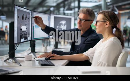 Two Engineers Working On Computer To Develop Car Gearbox Design. Stock Photo