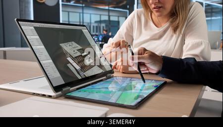 Two Architects Review 3D Building Model Together On Digital Tablet Screen. Stock Photo