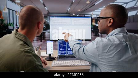 Young Software Engineer Uses Laptop And Desktop To Debug Mobile App. Stock Photo