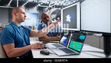 Two Young Engineers Use Computer Software To Design Solar Satellite. Stock Photo