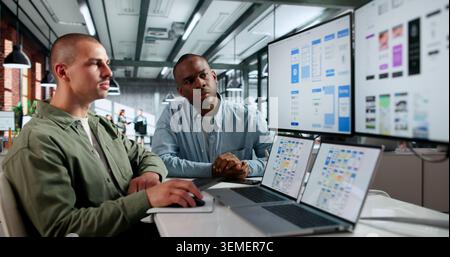 Two Young Male UX Designers Collaborate Online Using Laptops During Remote Webinar. Stock Photo