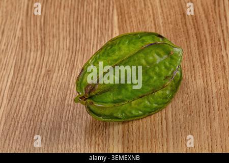 Single unripe carambola fruit resting on textured wood grain background. Vibrant green skin with natural ridges subtle brown spots Stock Photo