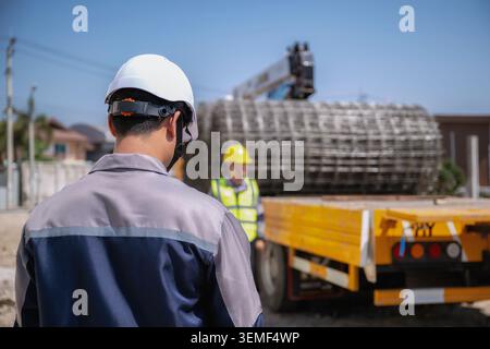 Asian engineer inspect wire mesh on the truck, Man wearing a white hard hat watches crane operations with copy space, Another worker in a yellow hard Stock Photo
