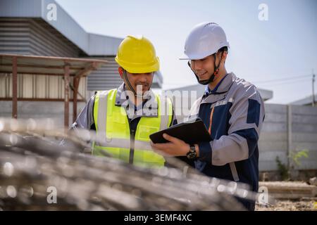 Asian engineer inspecting steel wire mesh construction site, Two builders raw material orders examine in tablet together, They examine coiled steel me Stock Photo