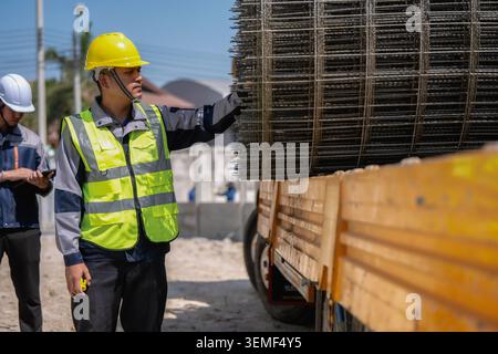 Asian builder inspect the wire mesh on the truck, construction worker in yellow hard hat gestures toward large metal mesh stacked on a truck with civi Stock Photo