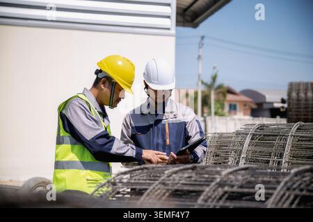Asian construction workers inspecting steel wire mesh construction site, Two construction workers checking material orders on tablet. They stand near Stock Photo