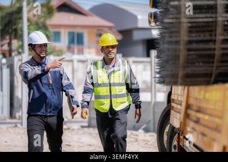 Asian two builder inspect wire mesh on truck, Construction workers walking and pointing to material on truck. One wears white hard hat and other wears Stock Photo