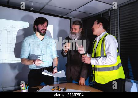smiling architects corporate investors holding coffee discussing blueprint success, after colleagues debate project details in a meeting room Stock Photo