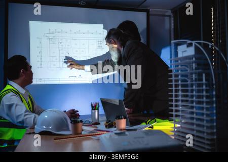 Engineering team discussing construction plan in dark meeting room, Construction manager explaining infrastructure plan with senior manager brainstorm Stock Photo