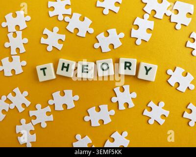Theory written with letter tiles, surrounded by scattered white puzzle pieces on a yellow surface Stock Photo