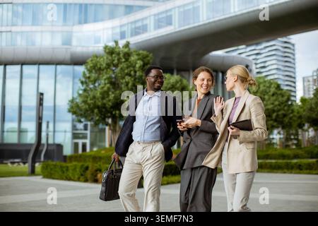 Three business professionals are walking together in a city park. They are smiling and engaging in conversation while enjoying the sunny weather and m Stock Photo
