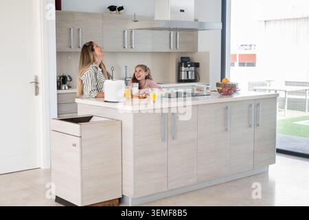 Happy mother and daughter sharing breakfast and spending quality time together in a bright modern kitchen at home. Family lifestyle concept with healt Stock Photo