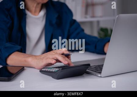 Close up senior woman hand using calculator and holding pen. Elderly lady calculating retirement pension, healthcare insurance budget, and paying bill Stock Photo