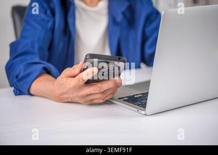 Close up of senior woman hands holding mobile smart phone. Elderly lady using laptop computer, browsing internet, checking social media app, or consul Stock Photo