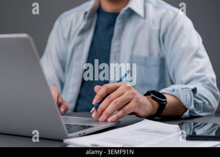 Close up creative designer man holding pencil and working on laptop computer. Freelancer student studying online course, planning business project wit Stock Photo