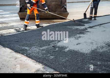 Workers repairing pavement at walking street in urban city, people laying fresh asphalt over sidewalk area using special tools Stock Photo