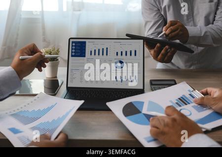 Business team reviewing accounting financial reports and dashboard charts on laptop and tablet during office meeting, supporting data analysis, budget Stock Photo