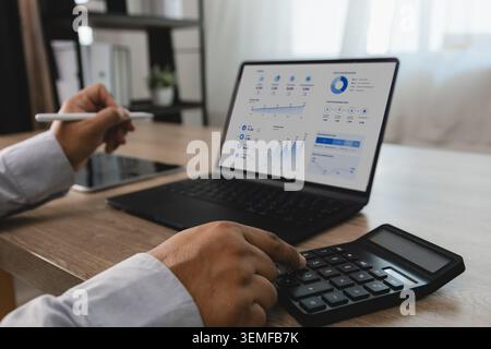 Person reviewing financial dashboard on laptop while using calculator and tablet at office desk, supporting accounting analysis, budget calculation, f Stock Photo