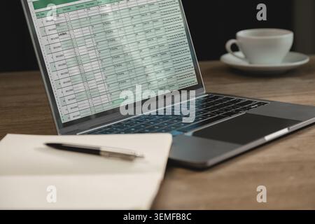 Laptop displaying spreadsheet dashboard with business data and project tracking table on workspace desk, supporting online analysis, financial reporti Stock Photo
