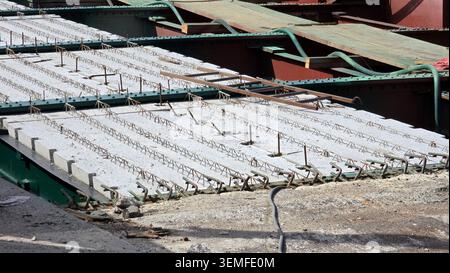 A close-up view shows prefabricated concrete structural slabs with exposed reinforcing steel lattices laid onto green and brown steel bridge beams Stock Photo