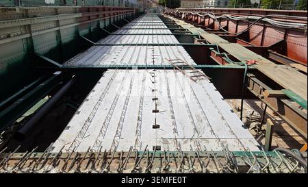 A long rows of precast concrete slabs with integrated lattice rebar sit secured within a massive steel girder bridge structure under construction Stock Photo